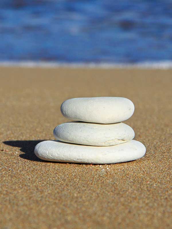 Aufeinandergetürmte, flache Steine an einem Sandstrand